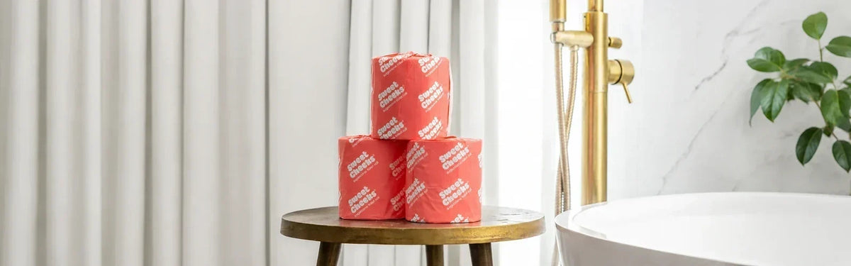 Stack of Sweet Cheeks sugarcane toilet rolls on a stool in a bright bathroom